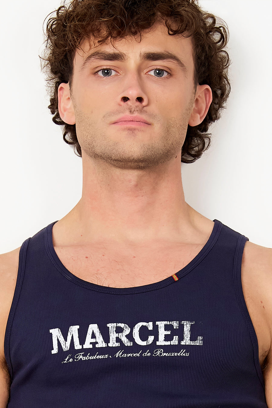 Débardeur côtelé bleu de Le Fabuleux Marcel de Bruxelles avec inscription blanche 'MARCEL' et une étiquette rayée à l'encolure.
