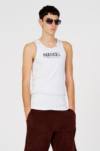 Débardeur blanc de Le Fabuleux Marcel de Bruxelles, avec un imprimé logo et porté avec un pantalon marron.