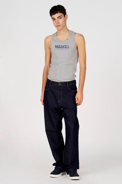 Débardeur gris de Le Fabuleux Marcel de Bruxelles, avec imprimé texte bleu sur la poitrine, porté avec un jean foncé et des lunettes de soleil.