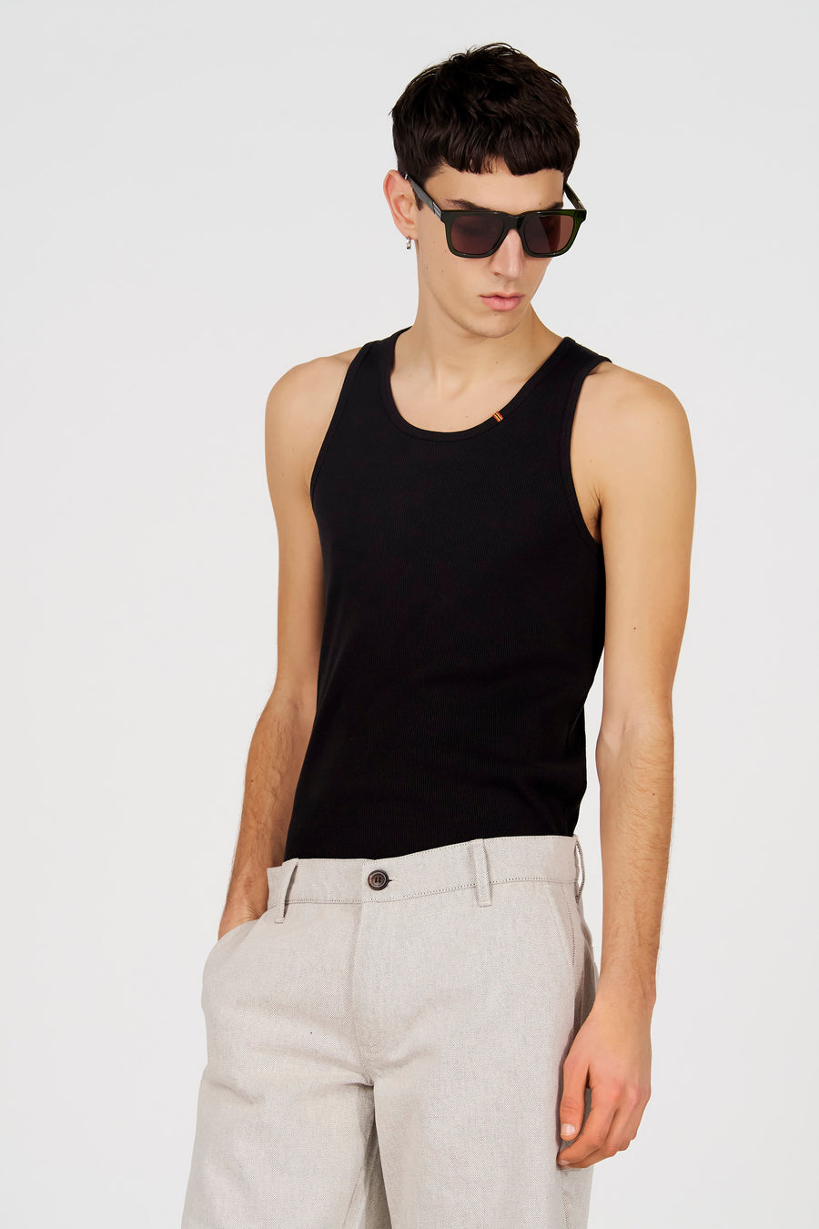Débardeur noir de Le Fabuleux Marcel de Bruxelles, porté avec un pantalon gris et des lunettes de soleil, debout.