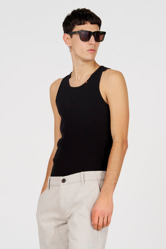 Débardeur noir de Le Fabuleux Marcel de Bruxelles, avec une texture côtelée, porté avec un pantalon beige et des lunettes de soleil.