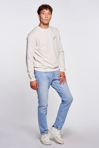 Jeans en denim bleu clair de Le Fabuleux Marcel de Bruxelles, portés avec un pull en crème et des baskets blanches.