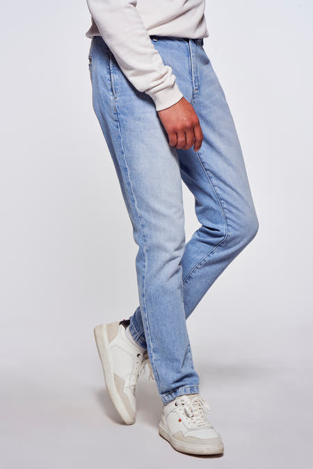 Jeans en denim bleu clair de Le Fabuleux Marcel de Bruxelles, avec des baskets blanches et un pull, dans une image coupée.