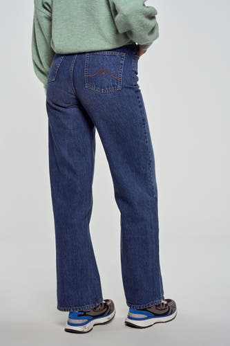 Donkerblauwe wijde jeans van Le Fabuleux Marcel de Bruxelles, met stiksels op de achterzakken, gecombineerd met een groene trui en sneakers.
