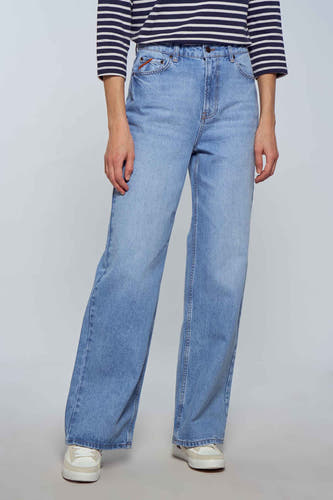 Jean bleu clair large de Le Fabuleux Marcel de Bruxelles, avec un haut rayé et des chaussures blanches.