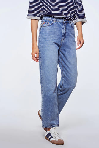 Personne en jeans bleus et chemise rayée, debout devant un fond blanc, avec des baskets.