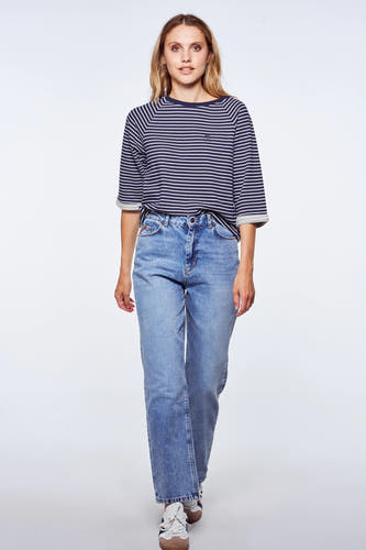 Femme, chemise rayée bleu et blanc, jeans bleus, baskets blanches.