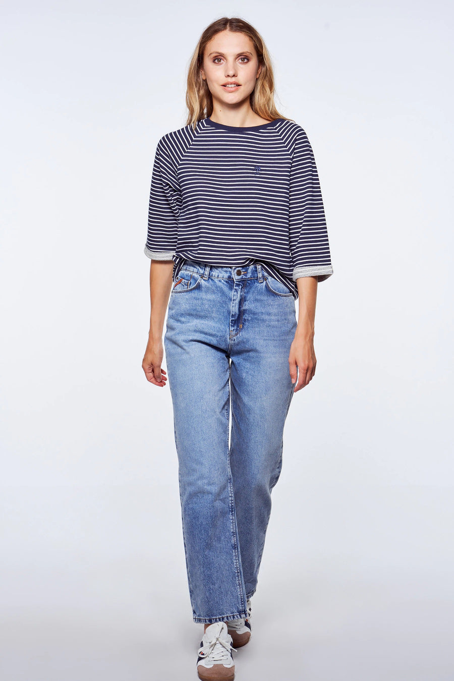 Femme, chemise rayée bleu et blanc, jeans bleus, baskets blanches.