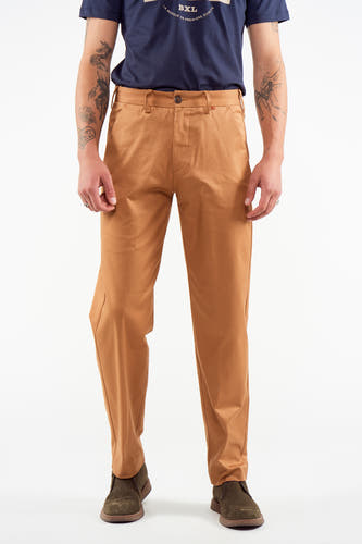 Pantalon de costume brun du Le Fabuleux Marcel de Bruxelles, porté avec un T-shirt bleu marine et des chaussures kaki.