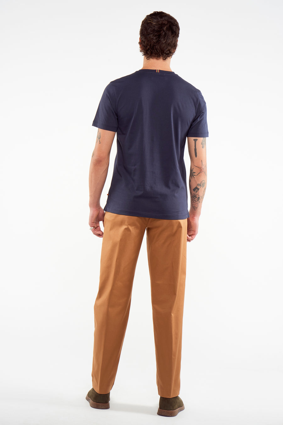 Pantalon de costume brun du Le Fabuleux Marcel de Bruxelles, avec des chaussures vertes et un T-shirt bleu marine.