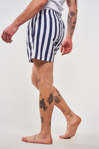 Pantalon bleu de Le Fabuleux Marcel de Bruxelles, avec des rayures verticales et des tatouages sur les jambes.