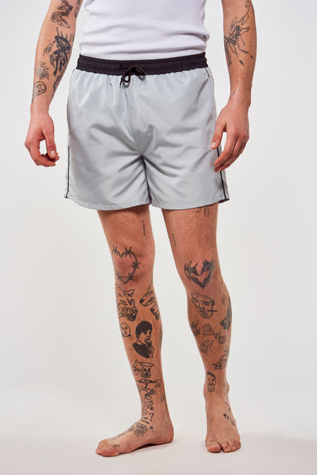 Pantalon bleu de Le Fabuleux Marcel de Bruxelles, vu de derrière, avec des tatouages sur les jambes.