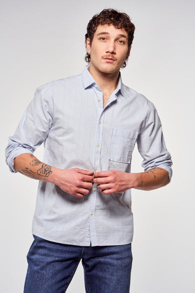 Chemise bleue rayée de Le Fabuleux Marcel de Bruxelles, manches longues, vue de derrière, associée à des jeans bleu marine.