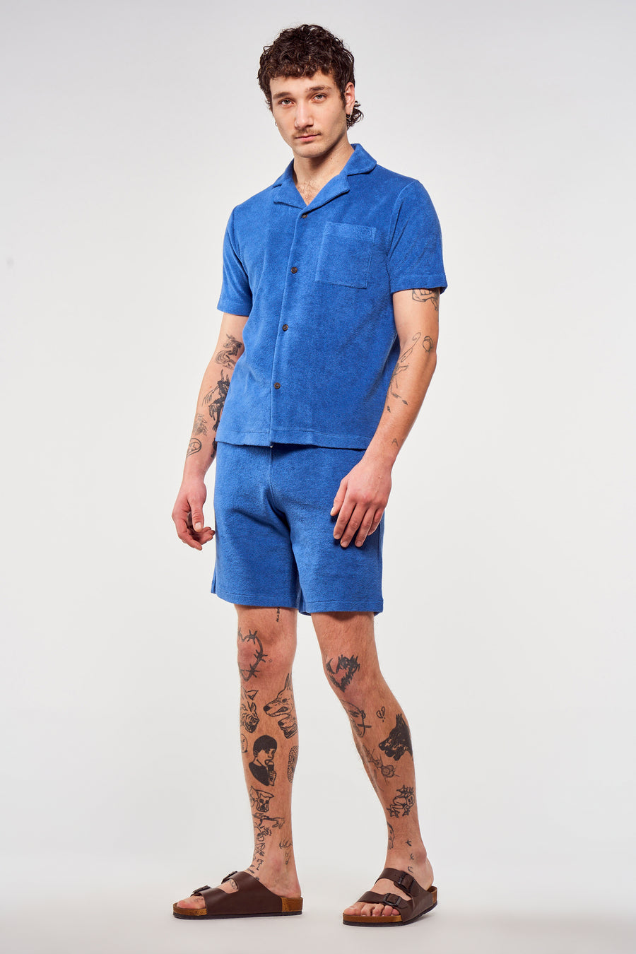 Short bleu de Le Fabuleux Marcel de Bruxelles, porté avec une chemise coordonnée et des sandales.