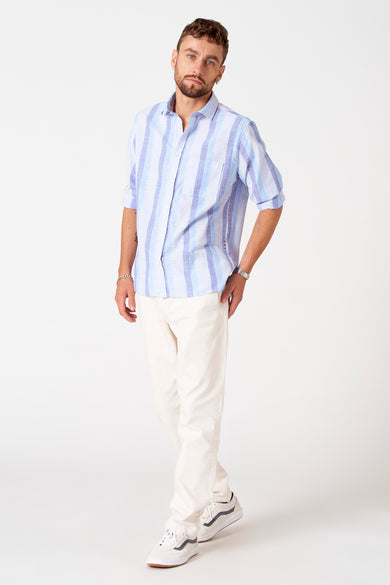 Chemise rayée bleue de Le Fabuleux Marcel de Bruxelles à manches courtes, associée à un pantalon crème clair et des baskets blanches.