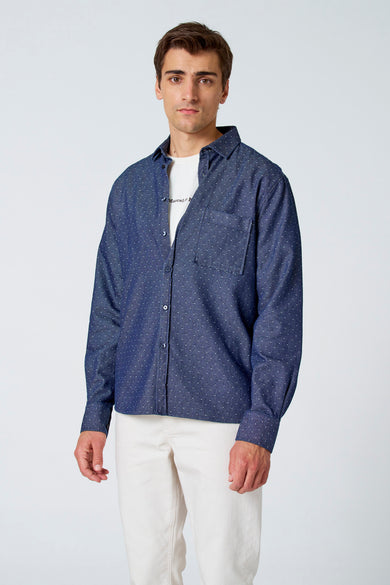 Chemise bleue à manches longues de Le Fabuleux Marcel de Bruxelles, à carreaux, portée avec un pantalon blanc.