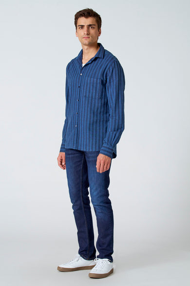 Chemise rayée bleue de Le Fabuleux Marcel de Bruxelles avec des manches longues, portée avec des jeans foncés et des baskets blanches, vue complète.