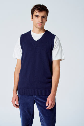 T-shirt bleu de Le Fabuleux Marcel de Bruxelles, à col en v, porté sur un chemisier rayé et une pantalon de corduroy bleu.