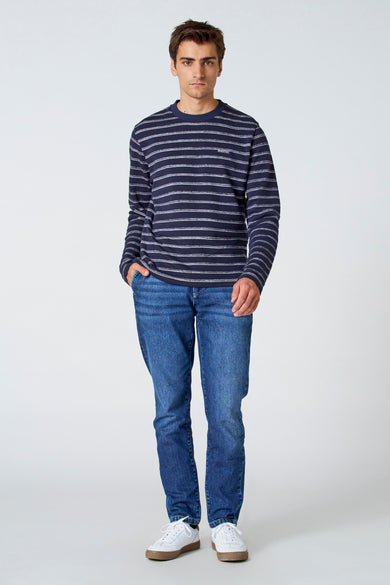 T-shirt blanc à manches longues de Le Fabuleux Marcel de Bruxelles, avec des rayures bleu marine horizontales et un jean.