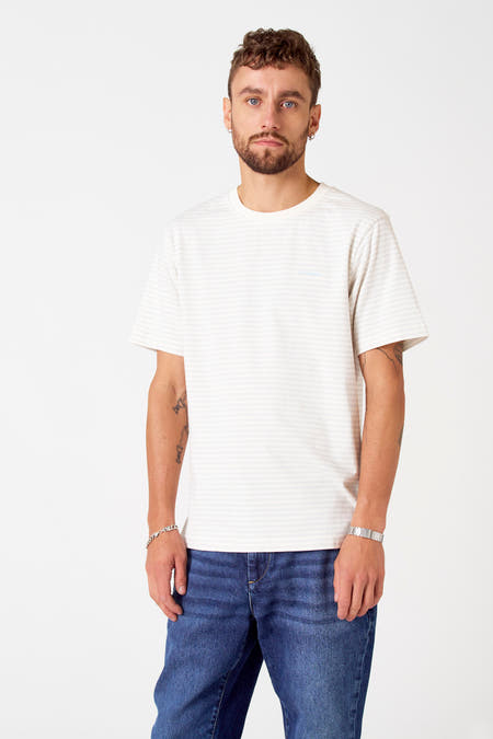 T-shirt gris à manches courtes de Le Fabuleux Marcel de Bruxelles, avec un motif rayé et porté avec des jeans et une montre.