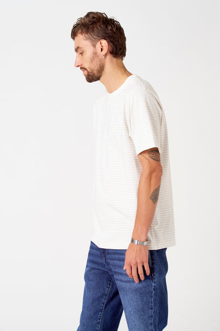 T-shirt gris rayé à manches courtes de Le Fabuleux Marcel de Bruxelles, avec une montre en métal et un jeans bleu marine.
