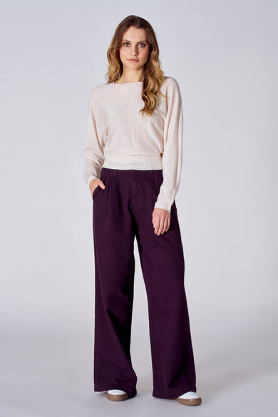 Pull blanc à col rond de Le Fabuleux Marcel de Bruxelles, associé à un pantalon violet avec des pinces larges.