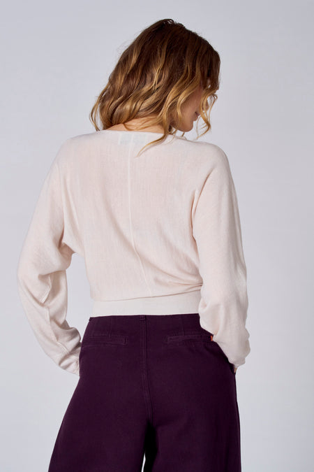 Pull blanc à col rond de Le Fabuleux Marcel de Bruxelles, avec des manches longues et un design simple, associé à une pantalon violet.