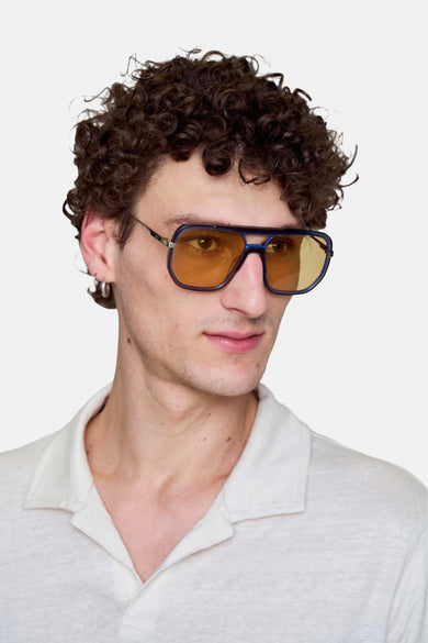 Lunettes de soleil bleues de Le Fabuleux Marcel de Bruxelles, avec des verres jaunes, portées par un modèle en chemise blanche.