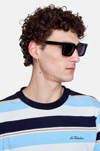 Lunettes de soleil bleues de Le Fabuleux Marcel de Bruxelles, portées par un homme en chemise rayée.