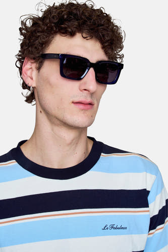 Lunettes de soleil bleues de Le Fabuleux Marcel de Bruxelles, portées par un modèle avec un t-shirt rayé.