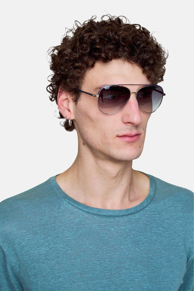 Lunettes de soleil couleur argent de Le Fabuleux Marcel de Bruxelles, portées par une personne aux cheveux bouclés et à un t-shirt bleu-vert.