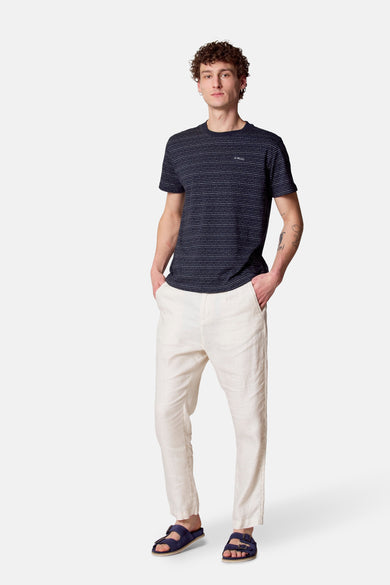 Pantalon de costume beige Le Le Fabux Marcel de Br Brelles, porté avec un chemisier rayé et des sandales bleues.