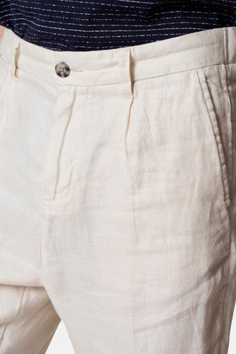 Pantalon costumier beige de Le Fabuleux Marcel de Bruxelles, avec plis et nœud, et une chemise rayée bleu foncé.