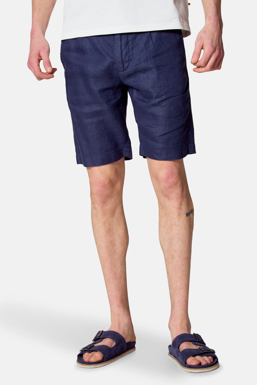 Man draagt blauwe linnen shorts en suède sandalen.
