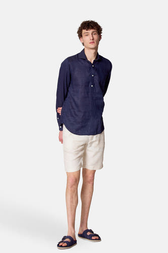 Chemise bleue à manches longues de Le Fabuleux Marcel de Bruxelles, portée avec des shorts en lin blanc et des sandales bleues.