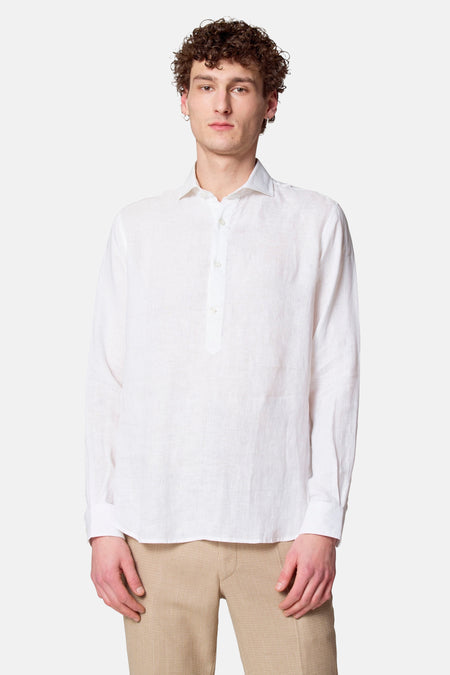 Een man in een wit linnen overhemd en beige broek staand voor een witte achtergrond.