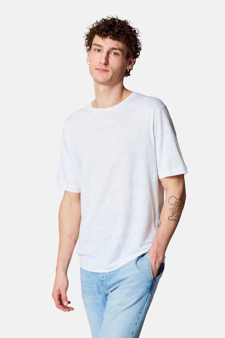 T-shirt blanc à manches courtes de Le Fabuleux Marcel de Bruxelles, porté avec un jean et un tatouage cartoon sur le bras.