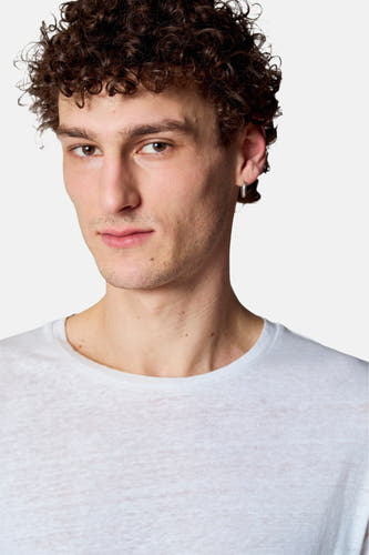 T-shirt blanc à manches courtes de Le Fabuleux Marcel de Bruxelles, porté par un homme aux cheveux bouclés et une boucle d'oreille en argent.