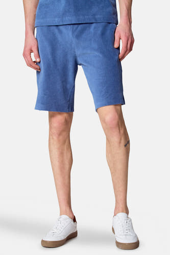 Short de corduroy bleu de Le Fabuleux Marcel de Bruxelles, porté avec des baskets blanches et un t-shirt bleu.