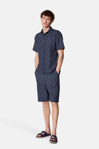 Chemise à fleurs bleues de Le Fabuleux Marcel de Bruxelles, avec des shorts et des sandales bleues assortis.