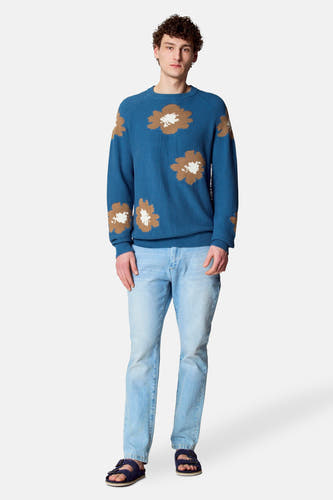 T-shirt bleu avec col rond de Le Fabuleux Marcel de Bruxelles, imprimé de fleurs brunes et blanches, associé à des jeans légers et des sandales.