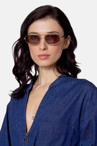 Lunettes de soleil dorées de Le Fabuleux Marcel de Bruxelles, portées par une femme en jumpsuit denim bleu.