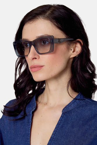 Lunettes de soleil bleues de Le Fabuleux Marcel de Bruxelles, portées avec un t-shirt denim bleu et une petite étoile tatouée sur l'oreille.