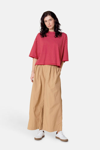 Vrouw met rode gestreepte top en wijde beige broek, staand op witte sneakers.