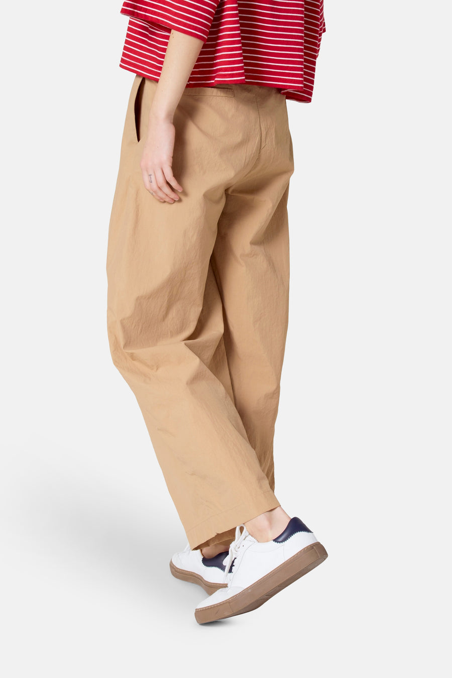 Persoon in khaki broek, gestreept rood-wit shirt en witte sneakers met bruine zool.