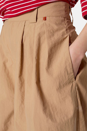Geplooide, khaki broek met hand in zak, rood-wit gestreepte top.