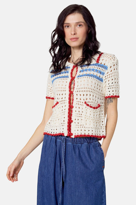 Pull beige à manches courtes de Le Fabuleux Marcel de Bruxelles, avec des rayures bleues et rouges et un pantalon de denim large.