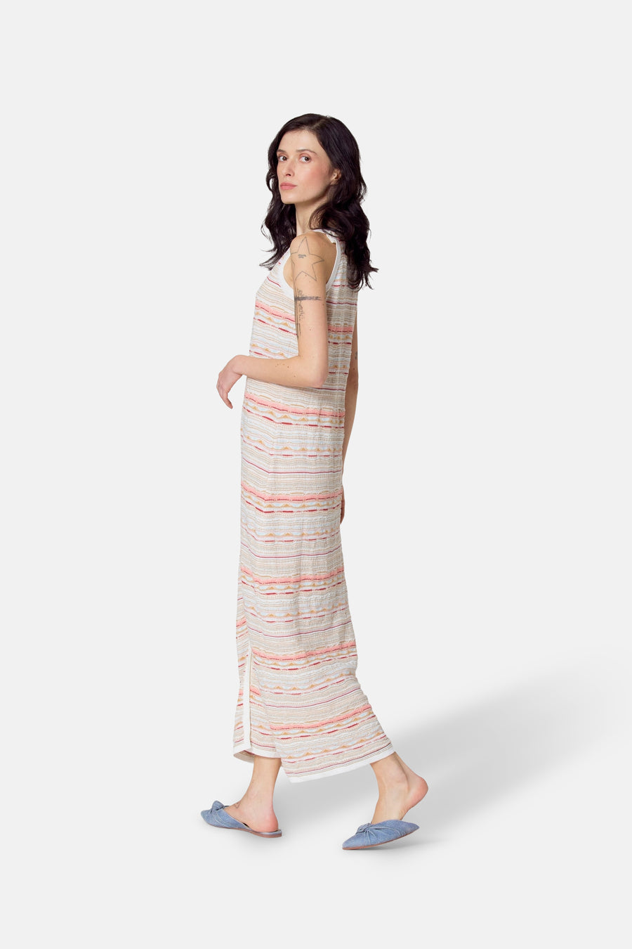 Vrouw in gestreepte, mouwloze maxi-jurk met blauwe slippers.