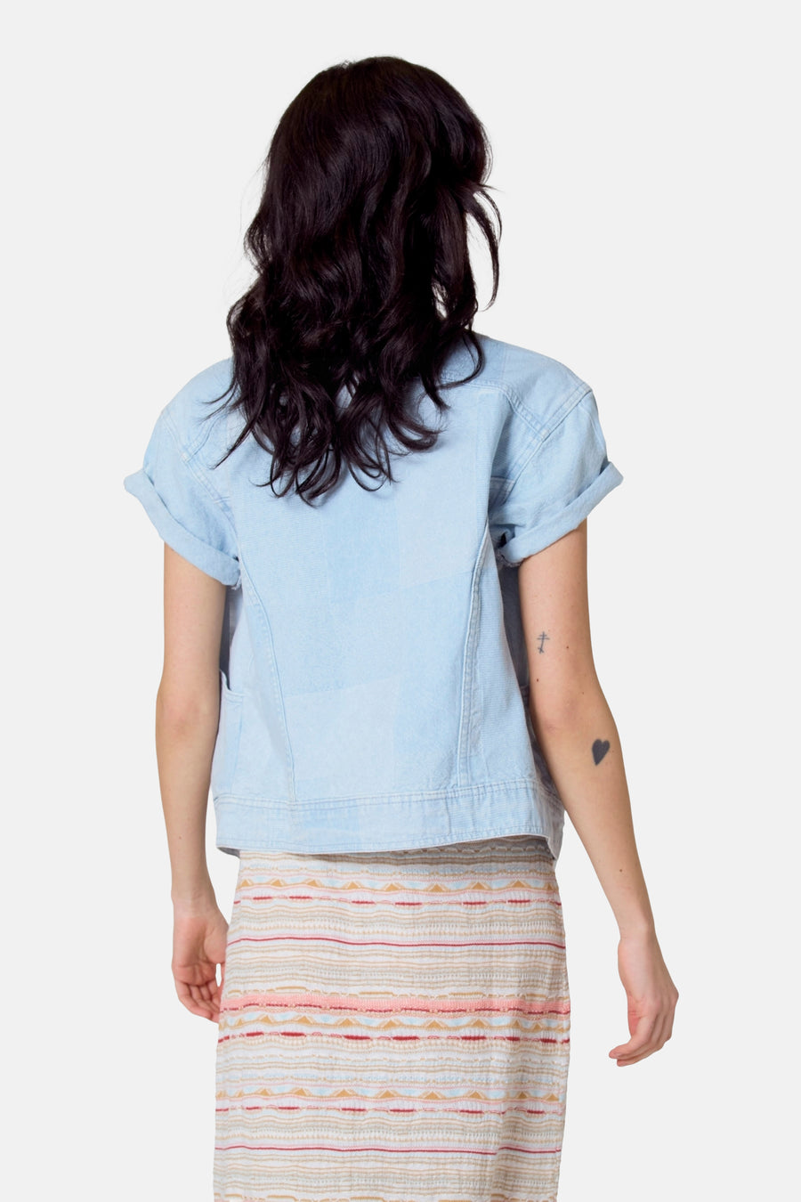 Lichtblauwe jeansjas van Le Fabuleux Marcel de Bruxelles, gezien van achteren, met opgerolde mouwen en een rok met etnisch patroon.
