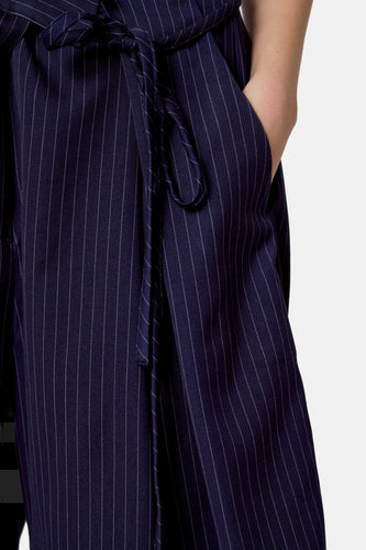 Close-up marineblauwe gestreepte broek met strik en hand in zak.